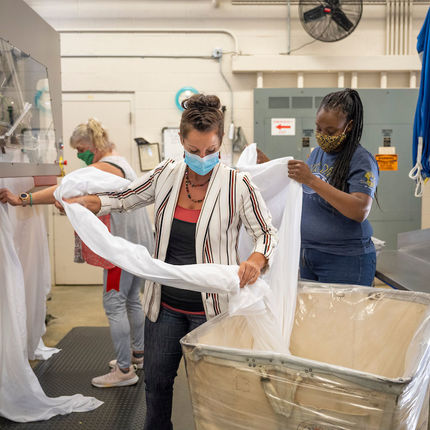 Jessica Jordan, production manager, (front center) helps Karen Fulford (right) and Karen Qureshi iron table linens at St. Michael's Laundry. (Photo by Barbara Johnston/University of Notre Dame)