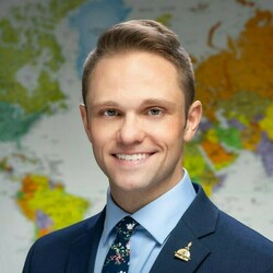 Cory Hankins, wearing a blue suit and tie, smiles in front of a world map.