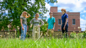 A group of students poses in a field with a brick building in the background.