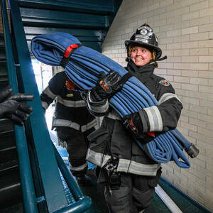 A firefighter carries hose up stairs.